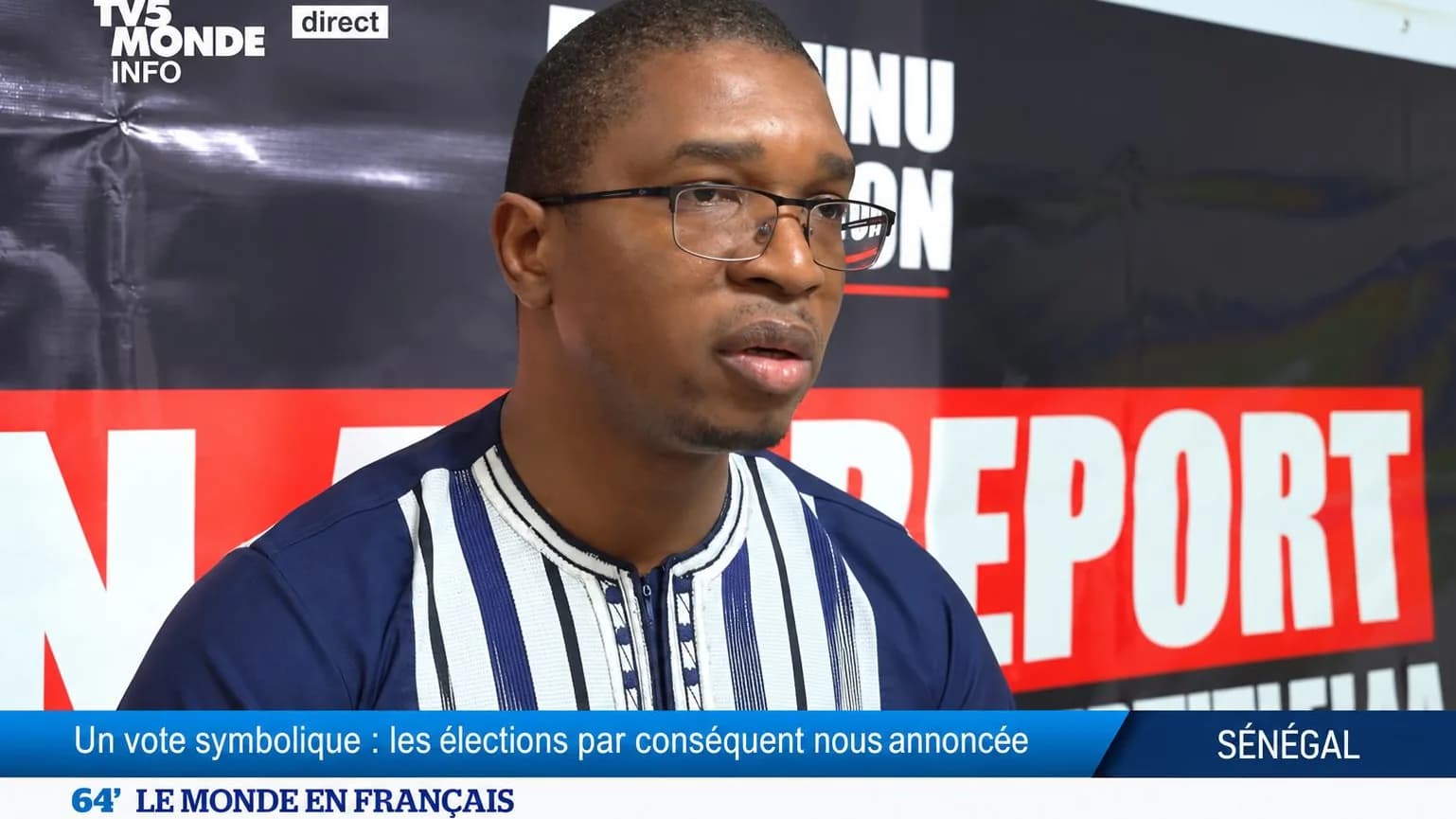 Jean Aimé interrogé sur le plateau de TV5MONDE, devant un fond « Report » barré de rouge